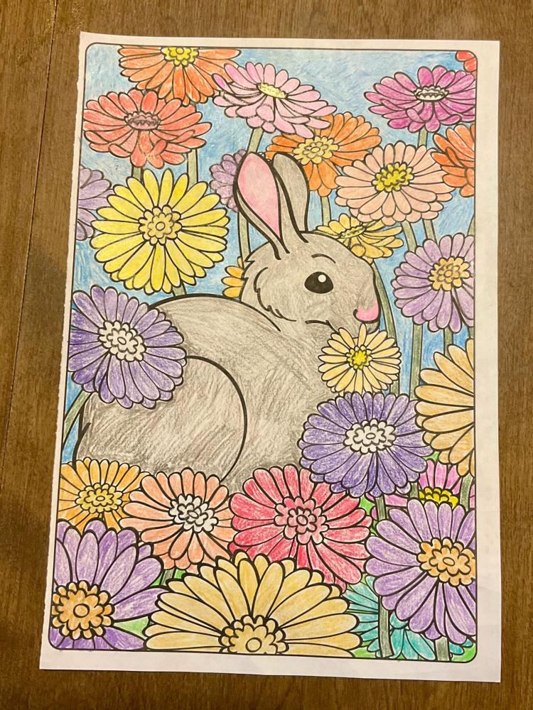 Gray rabbit among colorful flowers, including pink, yellow, and purple blooms.